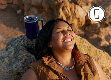 Girl leaning against a rock while smiling with her Thrive Mug sitting easily on the rock behind her.