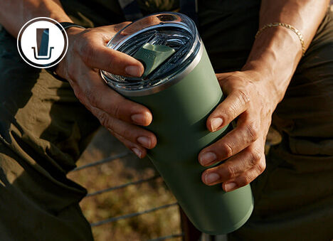 A person holding a Moss green Thrive tumbler with both hands.