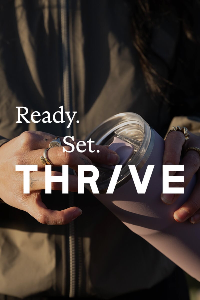 A closeup of someone holding a Thrive Tumbler with the words "Ready. Set. Thrive" on top
